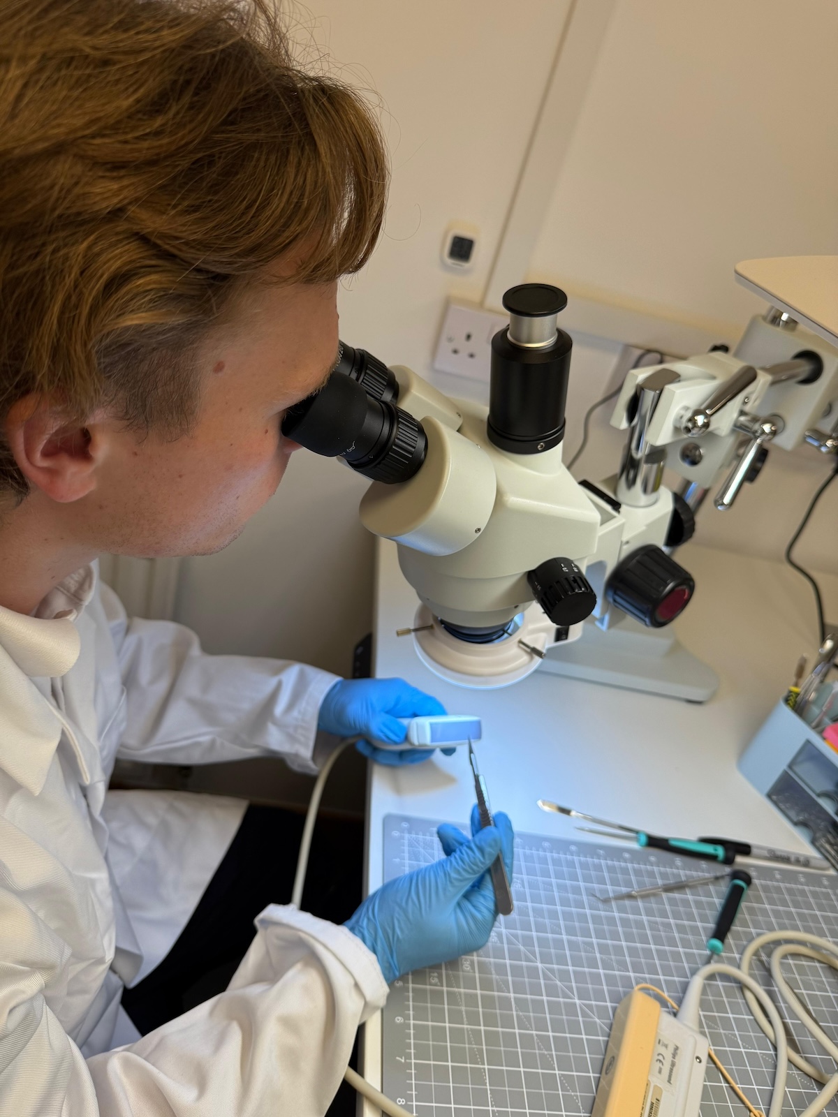 A technican repairing an ultrasound machine under a microscope using professional tools